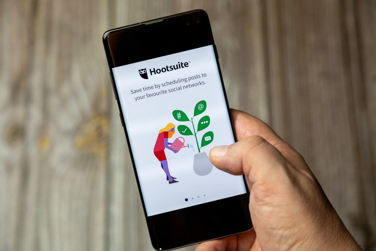 Eine Person hält ein Smartphone, auf dem die Hootsuite-Startseite zu sehen ist.